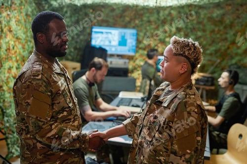 Preview: Two young intercultural officers in camouflage uniform shaking hands