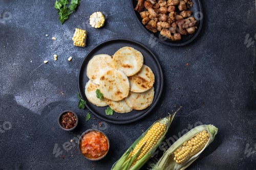 Preview: COLOMBIAN FOOD. Maize AREPAS and fried pork chicharron ans colombian tomato sauce. Top view. Black