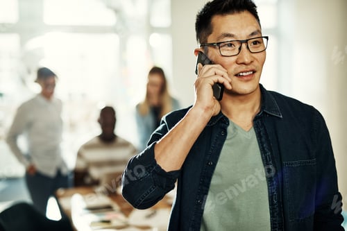 Preview: Young Asian designer talking on a cellphone in an office