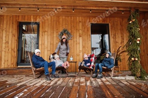 Preview: Attractive mother with her four kids on the terrace of a wooden house in winter day.