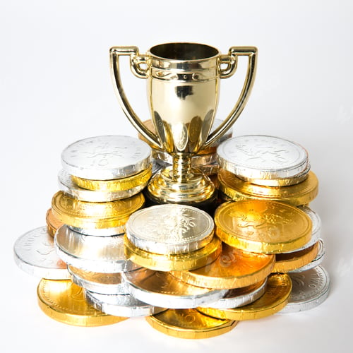 Preview: A gold winner’s trophy surrounded by a cash prize of gold and silver coins on white background
