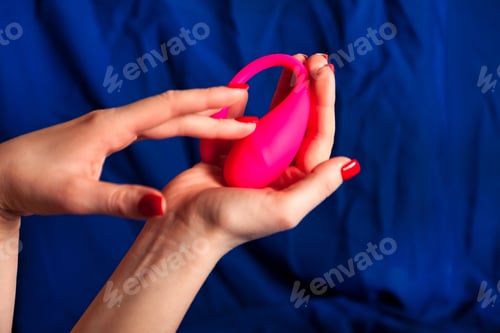 Preview: Woman Holds Pink Adult Sex Toy in Her Hand Against Blue Background
