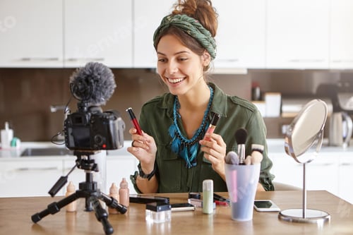 Preview: Young pretty female vlogger showing new kind of lipstick during recording vlog sitting at home. Woma