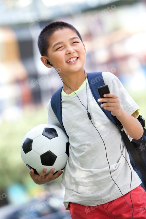 Preview: Schoolboy listening to MP3 player with football in hand