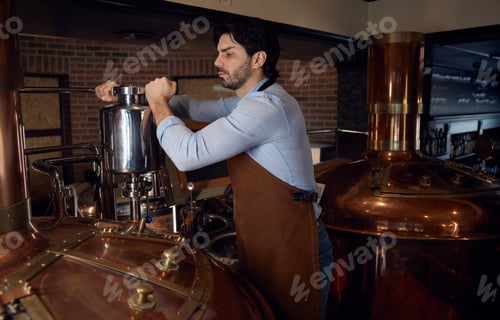 Preview: Brewer man wearing an apron is diligently working in a brewery setting