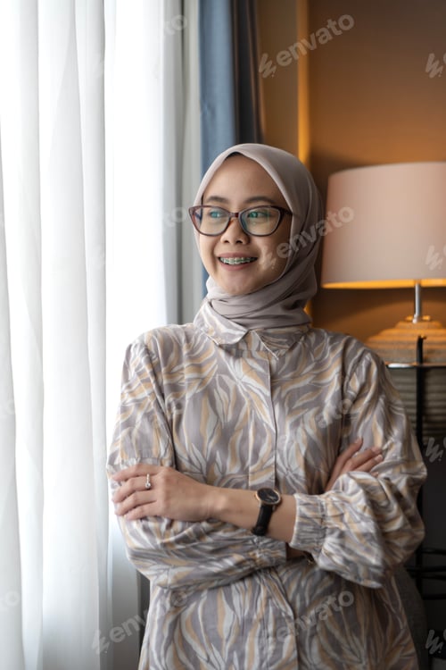 Preview: Asian Indonesian Muslim Woman with Hijab Looking Out Window Indoors