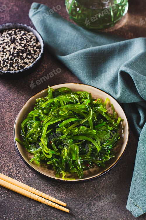 Preview: Delicious wakame seaweed salad on a plate and sesame seeds in a bowl on the table vertical view