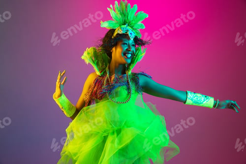 Preview: Beautiful young woman in carnival and masquerade costume on gradient studio background in neon light