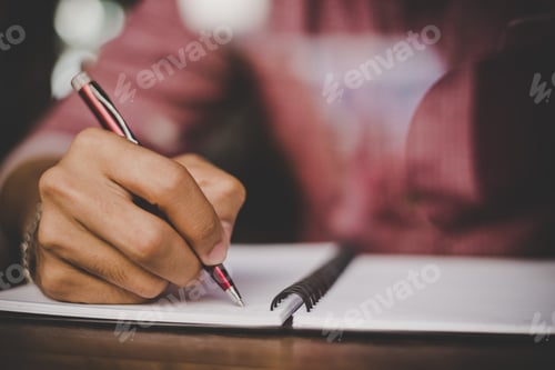 Preview: Hipster right hand writing on notebook in morning time with vintage film filter effect.