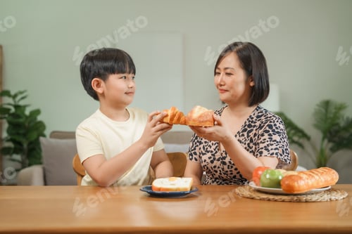 Preview: A mother and son happily feed each other snacks while sitting the table in their house.They share