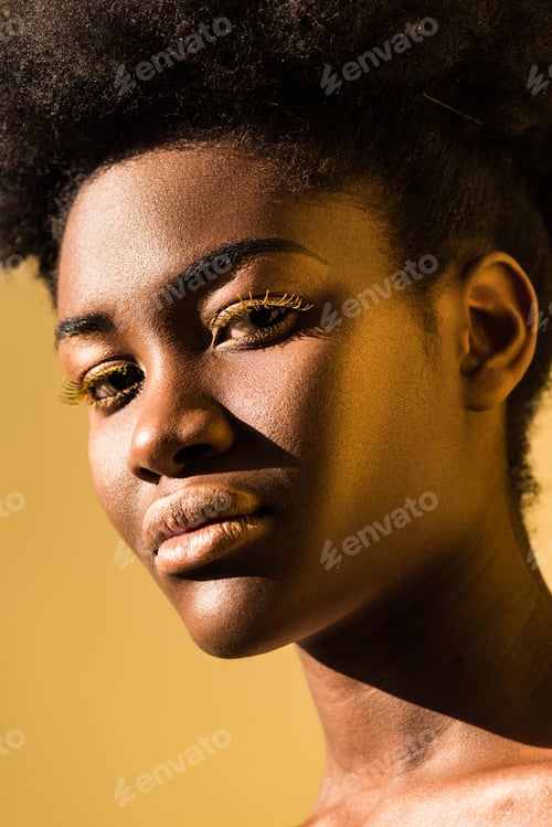 Preview: beautiful african american woman with yellow eyelashes looking at camera isolated on brown