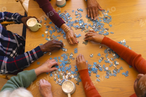 Preview: Hands of diverse group of senior friends playing with jigsaw puzzles in sunny dining room at home