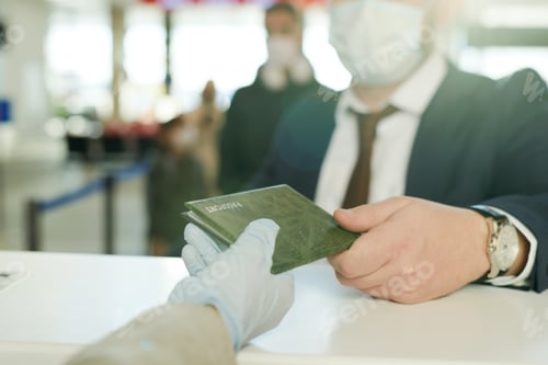 Preview: Gloved hand of female receptionist giving back passport of businessman over reception counter