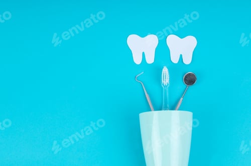 Preview: Dental Care Concept with Toothbrush, Mouth Mirror, and Probe in Cup Below Paper Teeth Cutouts