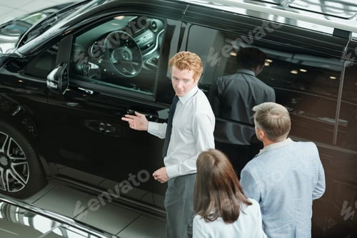 Preview: Young sales manager showing new model of car and describing it to consumers