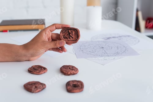 Preview: cropped view of predictor holding clay rune near star charts and blurred candles
