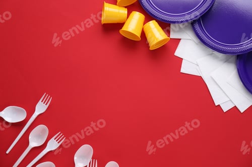 Preview: Set of disposable plastic tableware and paper napkins on red background, flat lay. Space for text
