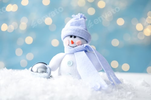 Preview: Snowman toy and Christmas ball on snow against blurred festive lights, closeup