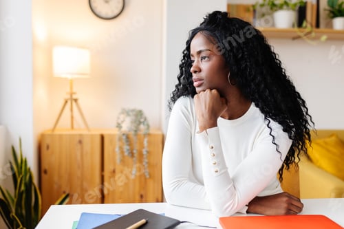 Preview: Thoughtful young black woman with laptop looking away while thinking at home