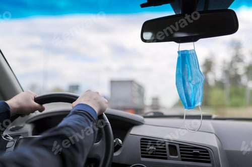 Preview: Protective medical mask of driver in car, mans hands on the steering wheel