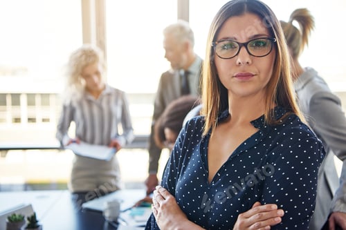 Preview: Focused young businesswoman with coworkers talking in the background