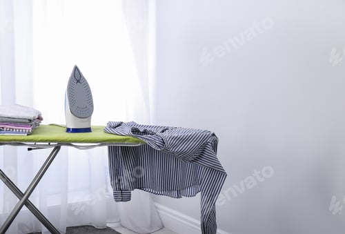 Vista previa: Modern electric iron and clothes on board indoors, space for text. Laundry day