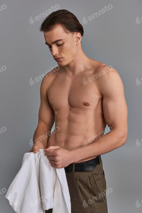 Preview: alluring attractive young man in brown pants posing topless on gray background and looking away