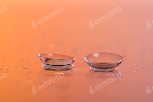 Preview: Pair of contact lenses and water drops on color gradient mirror surface, closeup