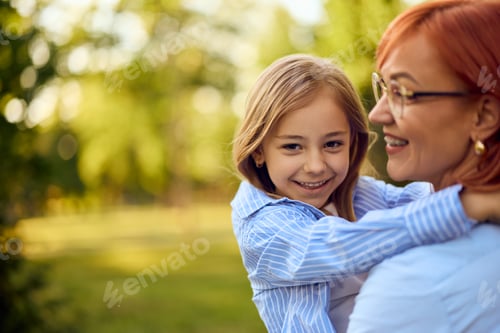Preview: Photo of a cute little girl in her mom's hands, smiling for the camera, at the park.