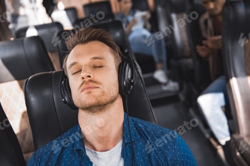 Preview: handsome male tourist in headphones listening music and sleeping during trip on bus