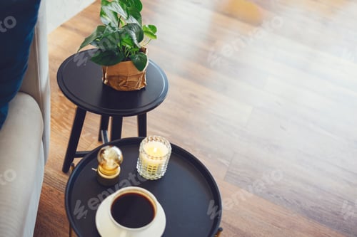Preview: Large white cup of coffee and lit scented candle on round black coffee table.