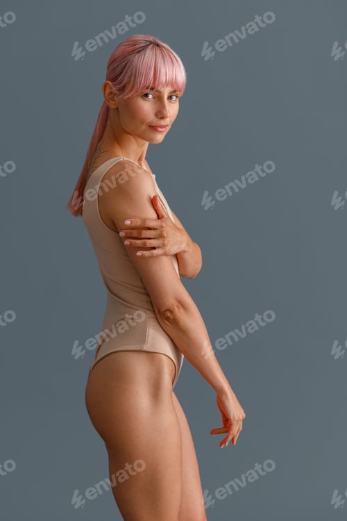 Preview: Attractive young woman with pink hair in beige bodysuit looking at camera, standing isolated over