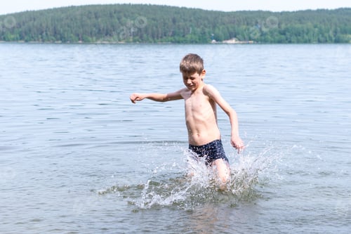 Preview: Cute happy boy makes water splash in the lake. The child runs through the water creating splashes