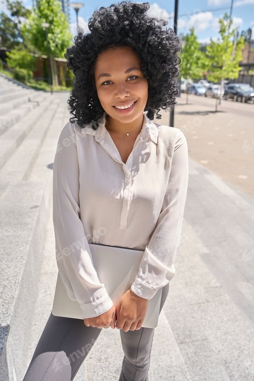 Preview: Multiracial woman standing on the stairs with a laptop in her hands
