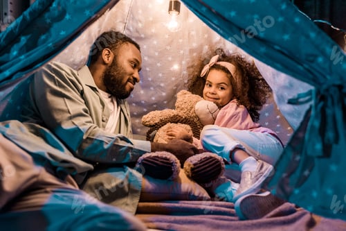 Preview: african american father looking at daughter in wigwam in living room