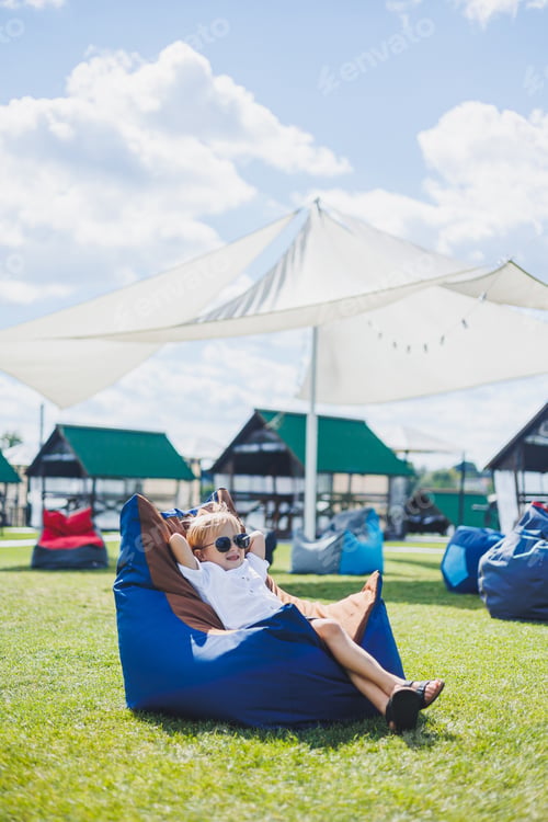 Preview: A fair-haired boy of 5-6 years old in a white T-shirt and shorts is sitting on a bean bag chair