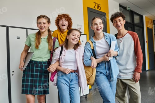 Preview: teenage schoolkids looking at camera and standing in school hallway, teen classmates with devices
