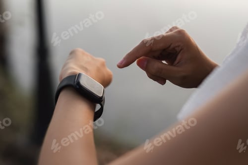 Preview: Young Asian woman uses smart watch while jogging at the park.