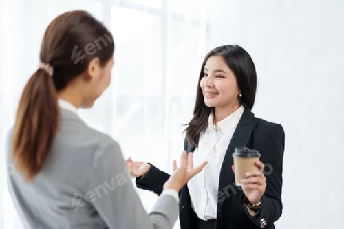 Preview: Two beautiful Asian business women standing chatting during a break relaxing coffee, discussing work