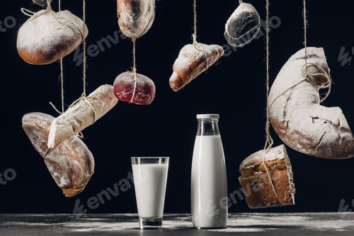 Preview: milk on table and bread with flour hanging on strings isolated on black