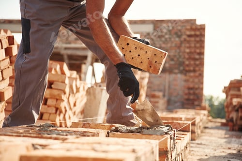 Preview: With brick in hands. Close up view of man that is working on the construction site