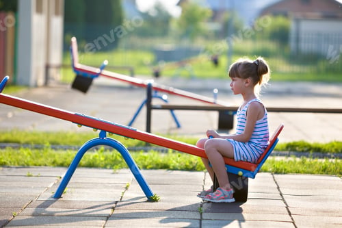 Preview: Cute young child girl outdoors on see-saw swing on sunny summer day.