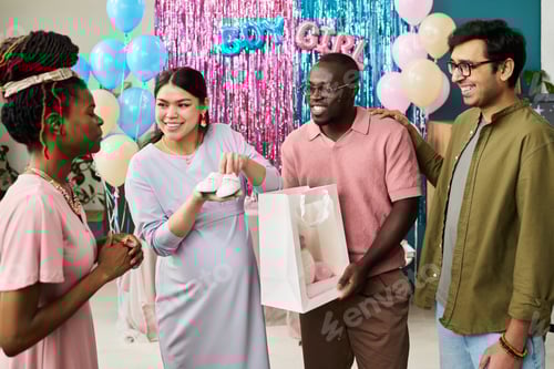 Preview: Pregnant young adult Asian woman holding baby shoes standing with smiling woman