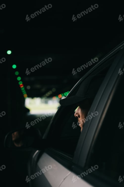Preview: male paparazzi in cap sitting in car and doing surveillance