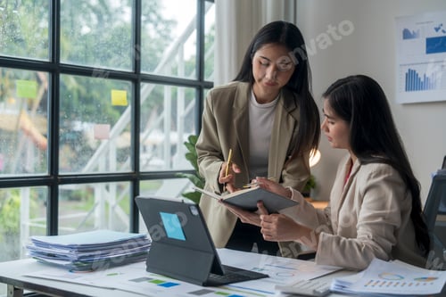 Preview: Two businesswomen having meeting analyzing financial charts and graphs using digital tablet