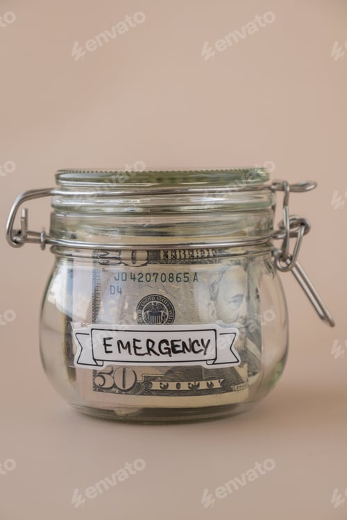 Preview: Saving Money In Glass Jar filled with Dollars banknotes. EMERGENCY transcription in front of jar