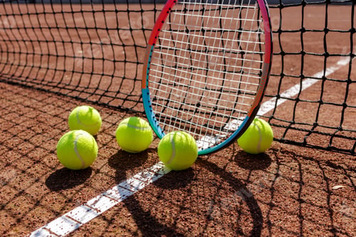 Preview: Tennis racket and balls on clay by the net training concept with strong shadow