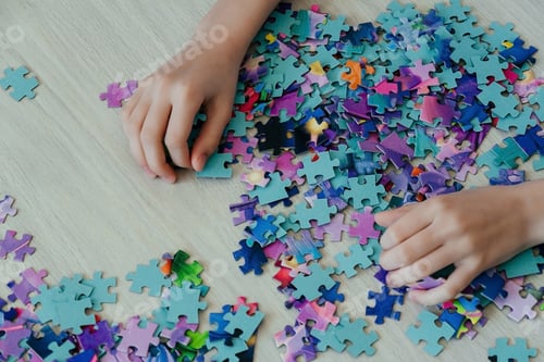 Preview: Caucasian girl collects puzzles on the table. Hands of a girl, top view
