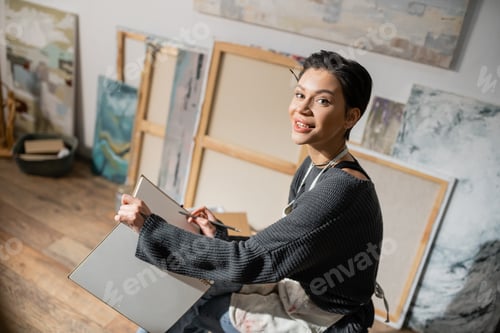 Preview: Young short haired artist holding pencil and sketchbook in studio