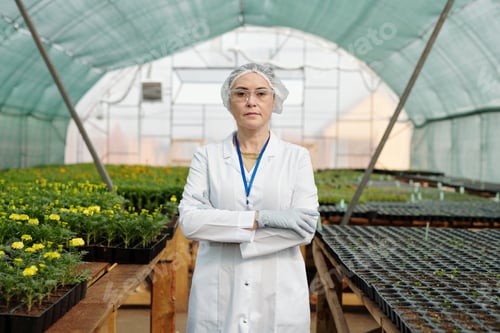 Preview: Confident scientific expert in protective workwear standing against tables with growing seedlings